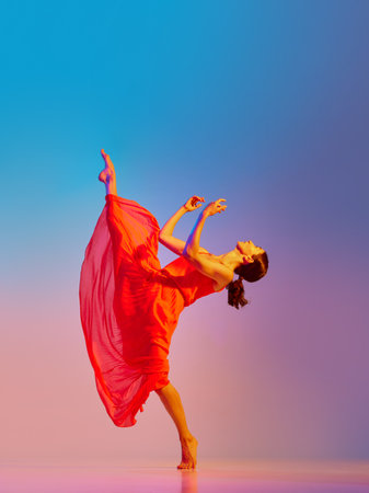 Elegant graceful young woman dancing in red dress against gradient multicolored background in neon light Stock Photo