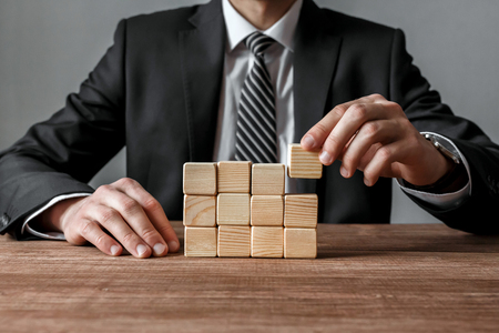 Businessman building a structure with wooden cubes on table success and business strategy concept Stock Photo