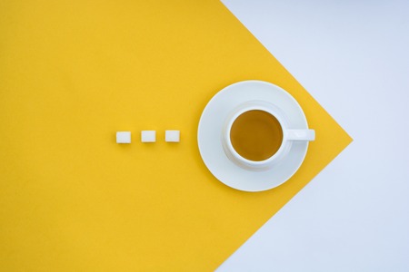 A cup of tea with three pieces of sugar on a yellow and white background