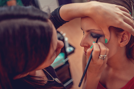 A portrait of a pretty woman having make up applied by a makeup artist close up