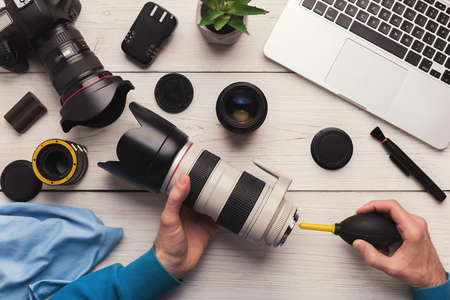 Camera lens cleaning with special tool close up photographer hands sweeping lens on workplace professional photographing equipment care technology concept