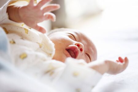 Newborn concept child on a white bed little kid relaxing at home newborn baby is fussing and crying close up