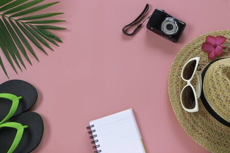 Flat lay top view with hat slippers camera notebook sunglasses flower and green leaf tropical palm for travel summer and holiday concept on soft pink background