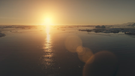 Vista aérea épica del atardecer en la Antártida, vuelo con dron sobre el agua del océano y el hielo de los glaciares, luz solar anaranjada con rayos brillantes