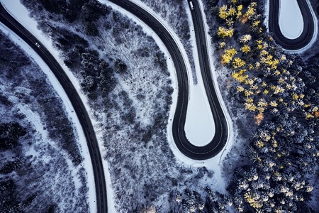 Aerial drone view of a curved winding road through the forest high up in the mountains in the winter with snow covered trees and curved streets in winter