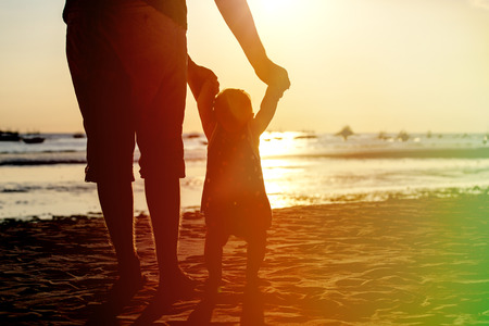 padre y la pequeña hija de aprendizaje para caminar en la playa de la puesta del sol