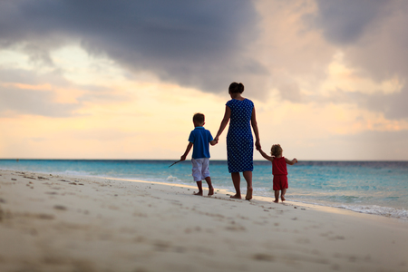 madre con pequeño hijo e hija caminando en la playa al atardecer