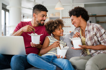 Feliz familia afroamericana comiendo en el sofá con cajas de cartón en el interior de la sala de estar Foto de archivo