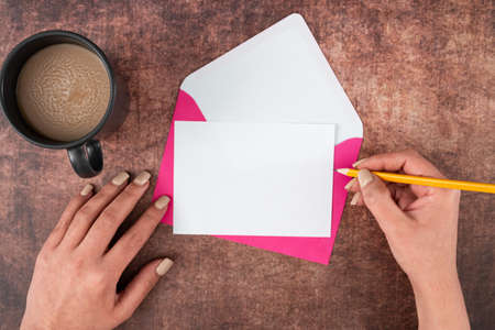 Manos de mujer con lápiz, papel en blanco, sobre y taza de café sobre fondo de madera. mujer de negocios bebiendo y escribiendo un mensaje crucial en una carta comercial.