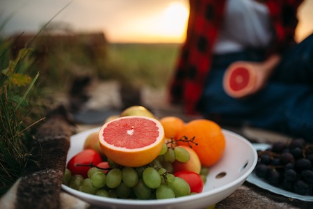 Female person with fruits sitting on plaid picnic