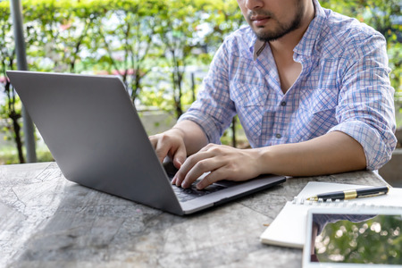 Businessman working with laptop on table man hands typing on notebook computer business person working on desk outdoor with green nature in background soft focus