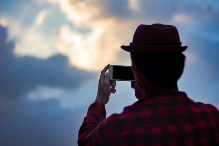 Young man taking photo of beautiful blue sky with mobile smart phone back view