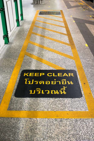 Mantenga una señal de advertencia clara en una cruz amarilla en el suelo en la estación de tren Sky, Bangkok, Tailandia. Con carácter tailandés que dice "manténgase alejado".