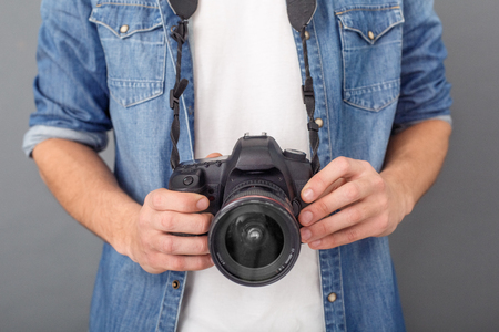 Young guy photographer wearing jeans jacket studio isolated on grey wall holding professional camera close up