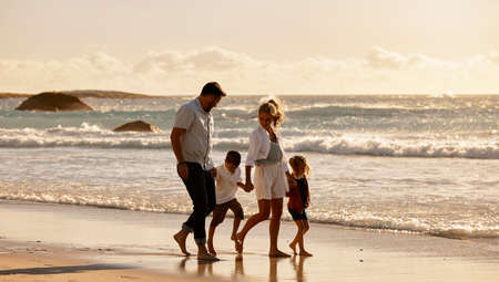 Familia caucásica despreocupada caminando juntos en la playa por la mañana, los padres pasan tiempo con su hijo y su hija mientras están de vacaciones, sus hermanos pequeños caminan con sus padres de vacaciones Foto de archivo