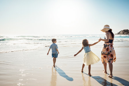 Divertida y brillante foto de vista trasera del verano de una madre uniéndose a sus dos hijos pequeños en la playa Foto de archivo