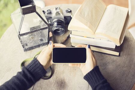 Girl hands with smartphone old camera and books on a wooden table