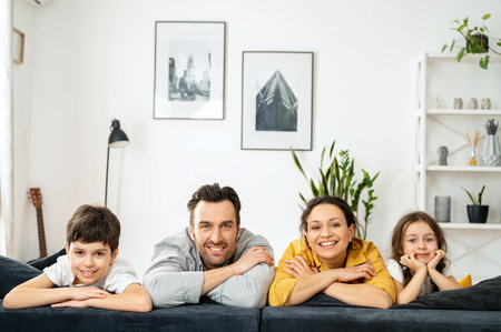 Feliz familia multirracial de cuatro personas tendidas en el sofá en una acogedora sala de estar, padres e hijos riéndose. Familia sintiéndose feliz durante el fin de semana