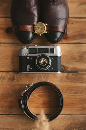 Wedding rings on an old camera shoes watch and belt mens attributes on the wooden floor