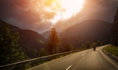 Motorcyclist in action bright red sunset light overcast weather active lifestyle traveling along alpine mountains extreme adventure concept Stock Photo