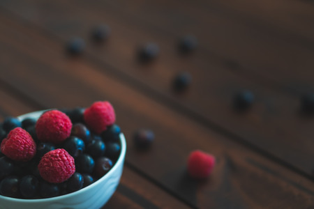 Bowl of blueberries and raspberries on a dark brown wooden table