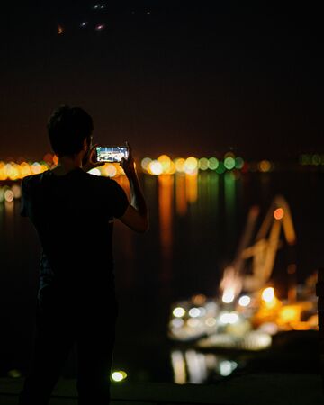 A man takes a photo of the night city on a smartphone shooting the city lights with a mobile device at night view through the screen at the time a man takes a photo of a city at night cityscape