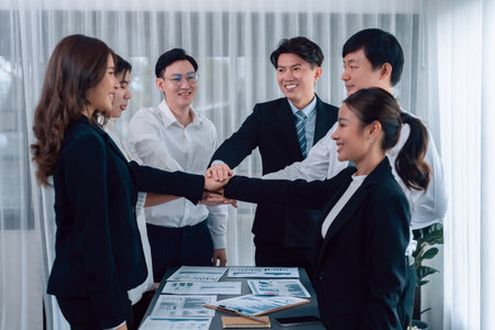 Closeup business team of suit clad businessmen and women join hand stack together and form circle colleague collaborate and work together to promote harmony and teamwork concept in office workplace