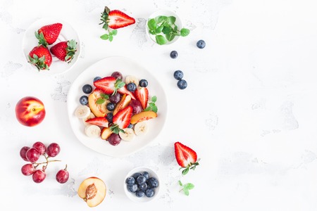 Fruit salad with strawberry blueberry peach banana grape and fresh fruits on white background flat lay top view copy space Stock Photo