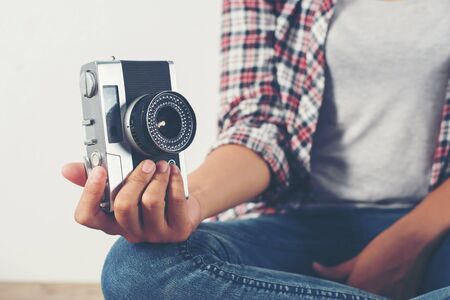 Young hipster photographer hand holding retro camera sitting on wooden floor