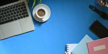 Top view image of computer laptop putting on colorful working desk with coffee cup potted plant pencils in glass vase smartphone note smartwatch and notebook orderly workspace concept