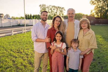 Gran familia de tres generaciones de pie sobre césped verde en el campo