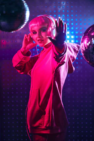 Dj girl attractive girl with bright glitter make up and pink hair poses with headphones in neon light of the nightclub showing a stop gesture night party disco girl