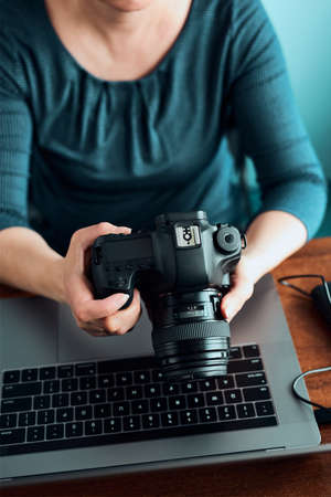 Female photographer working on photos on laptop and camera woman editing retouching browsing photos working as a freelancer sitting at desk