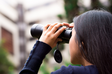 Young woman stalking with a black binoculars in a city background