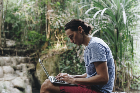 White man using computer laptop at waterfall