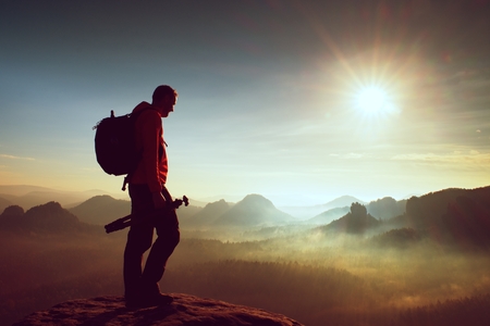 Tall adult photographer think about picture at sunset in the misty mountains