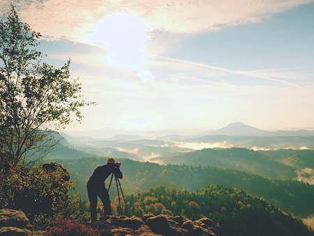 Nature photographer in the action man silhouette above a misty clouds morning hilly landscape Фото со стока