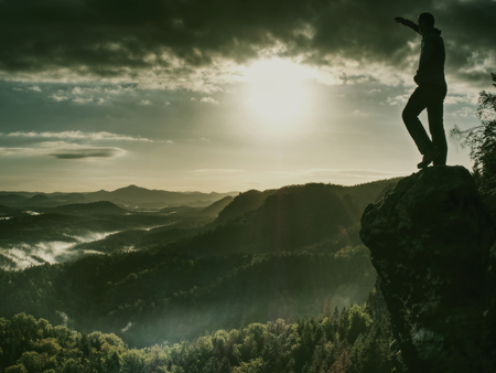 Sharp cliff edge with man watching over misty and foggy morning valley to cold sun hidden in clouds Stock Photo