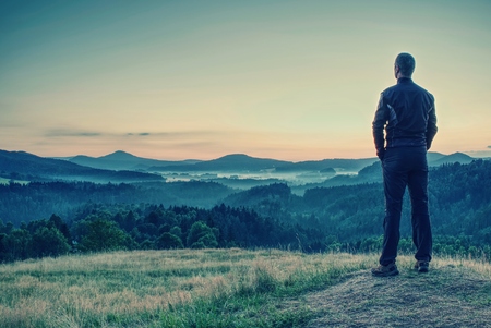 Man tourist traveler standing on cliff of mountain and looking to sunset against backdrop of hills concept active recreation in mountains