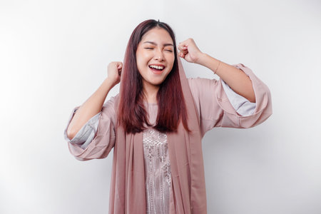 A young asian muslim woman with a happy successful expression wearing a hijab isolated by white background Фото со стока