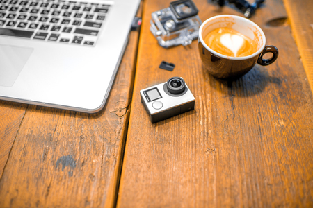 Small action video camera with coffe cup and laptop on the wooden table