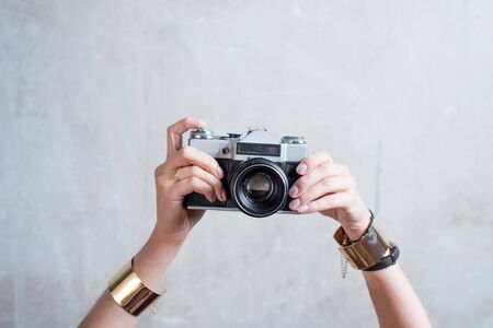 Female hands holding retro photo camera on the gray wall background