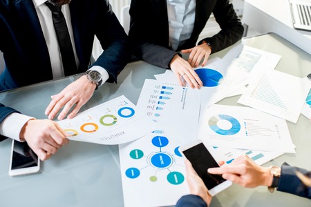 Business people working on paper charts and smartphones sitting at the table top view with no face