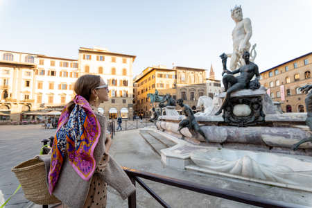 Giovane donna che viaggia famosi punti di riferimento italiani nella città di Firenze. Godendo della splendida architettura e della fontana del Nettuno in piazza della Signoria. Donna vestita in stile italiano con sciarpa colorata tra i capelli