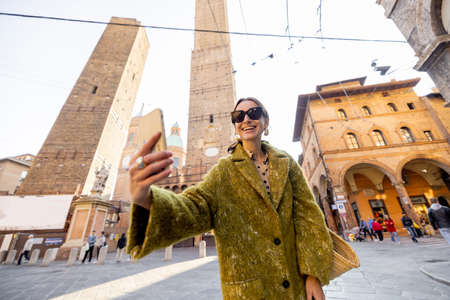 Giovane donna alla moda che scatta foto selfie sul telefono sullo sfondo delle famose torri degli Asinelli mentre viaggia nella città di Bologna. Concetto di visitare i punti di riferimento italiani nella regione Emilia Romagna Archivio Fotografico