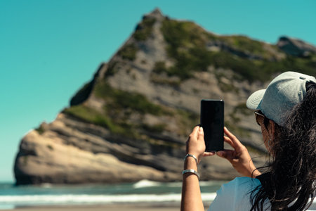Mujer tomando fotos con el móvil en la playa de Wharariki, Nueva Zelanda.