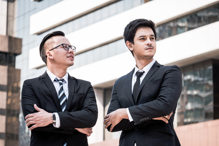 Portrait of two young asian businessmen in black suit standing with office building background Stock Photo