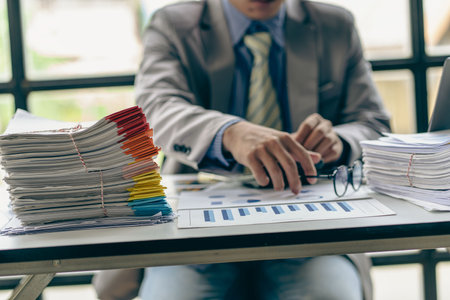 Businessman working in finance with pile of unfinished papers on the desk business paper pile