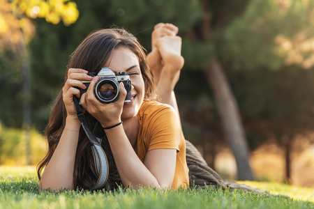 Smiling young woman using a camera to take photo at the park