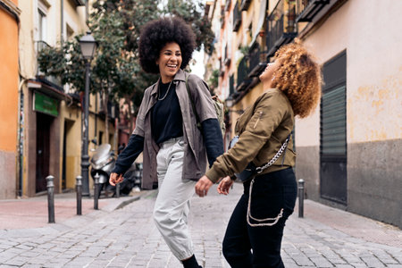 Fotografía de Stock de chicas afro felices e informales riendo y caminando por la ciudad